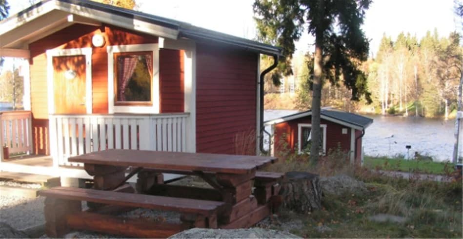 En mysig stuga med veranda omgiven av träd och grönska på Munkebergs Camping.