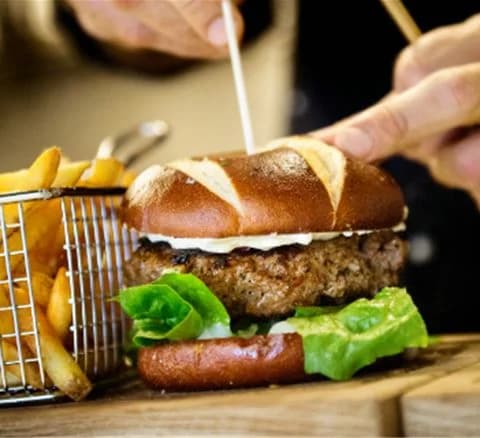 En hamburgare med kött, placerad på ett bord, omgiven av bröd och tillbehör, på Gustavsvik Resort.