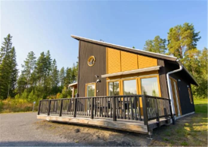En mysig timmerstuga med veranda bland grönskande träd på Skellefteå camping.