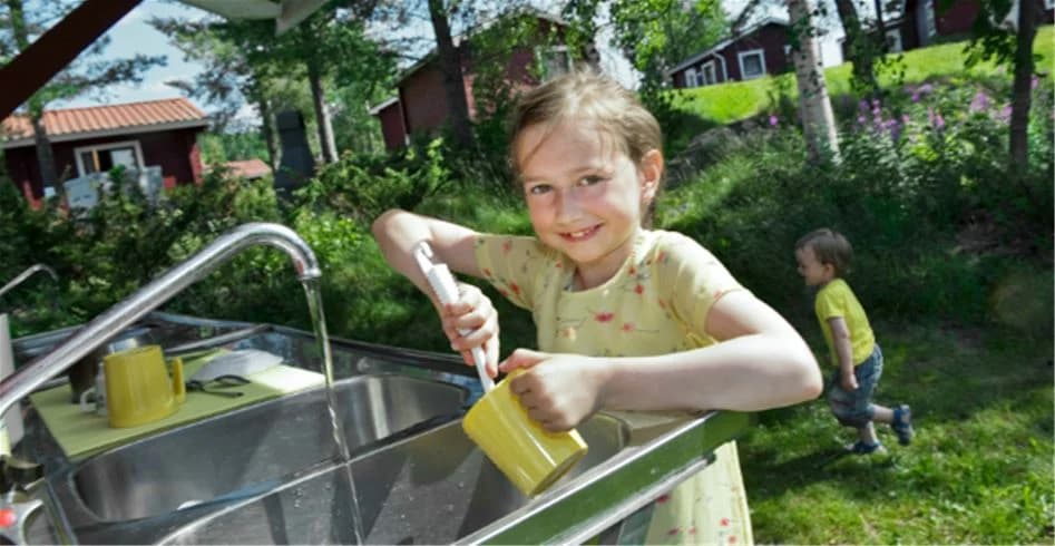 Ett barn leker i en trädgårdsmiljö med färgglada plastleksaker på Skellefteå camping under våren. Barnet ser ut att ha roligt i den gröna och rymliga utomhusmiljön.