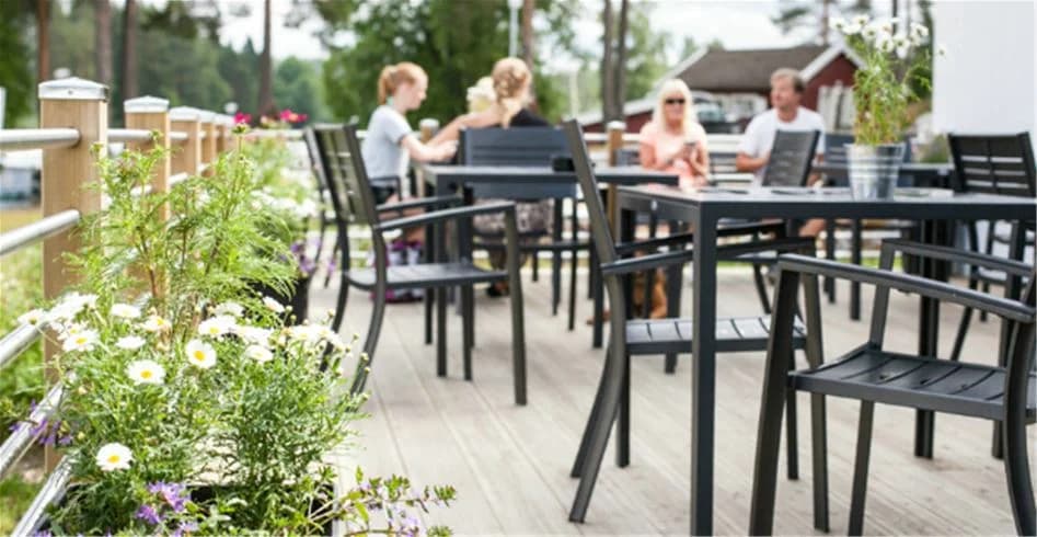 En utomhus restaurang på Skellefteå Camping med träbord och stolar under solskydd. Golvet är en trädeck.