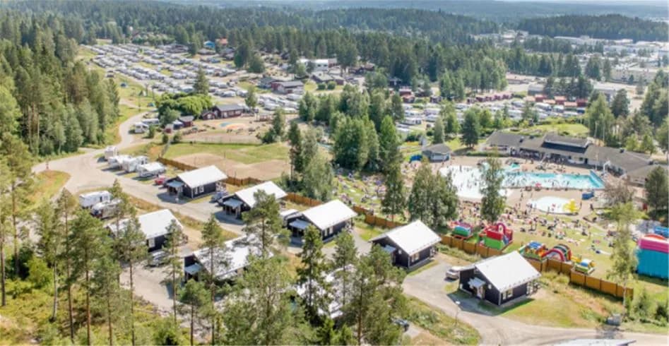 Flygbild över Skellefteå Camping, med en vy av trädkantade gångvägar, stugor, en swimmingpool och grönområden i en välplanerad och naturnära miljö.
