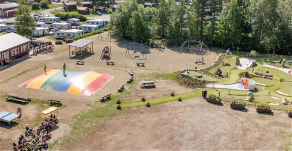 En lekplats med klätterställningar och gungor i en grönskande parkmiljö på Skellefteå camping.