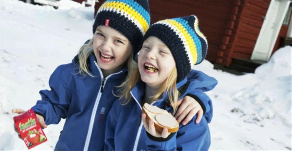 En glad person iklädd vinterjacka och stickad mössa ler mot kameran i ett snötäckt landskap vid Skellefteå camping.