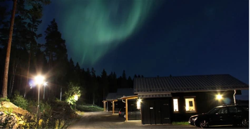 En nattbild av Skellefteå camping med stugor upplysta av säkerhetsbelysning, som skapar en inbjudande atmosfär i det omgivande mörkret.