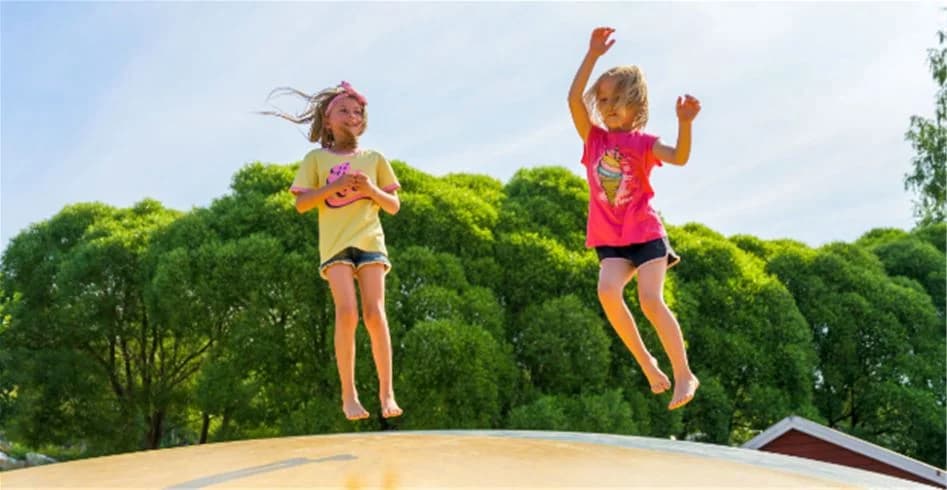 En glad grupp människor njuter av sommaren och leker utomhus på Skellefteå Camping. Flera barn hoppar på lekutrustning omgivna av en grönskande natur, vilket förmedlar en känsla av fritid och glädje.
