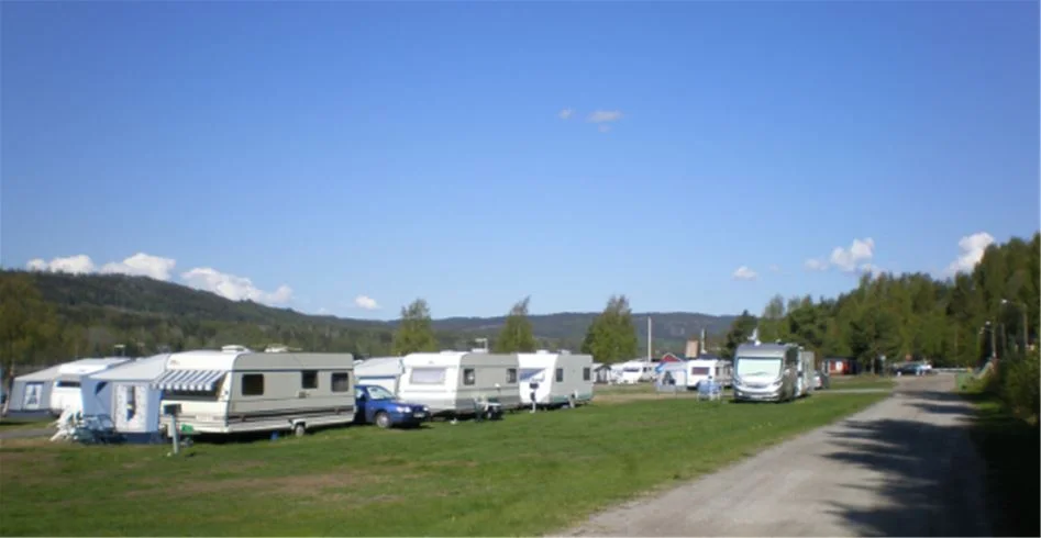 En campingplats med flera husvagnar och bilar parkerade på gräsytor, omgivna av grönska och träd.