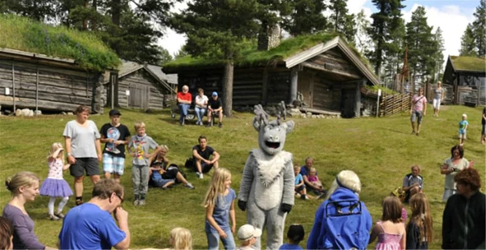 En familjevänlig campingplats vid Idre Fjäll med glada besökare som njuter av sin semester. Flera små stugor syns i ett naturskönt parkområde där både barn och vuxna deltar i olika fritidsaktiviteter.