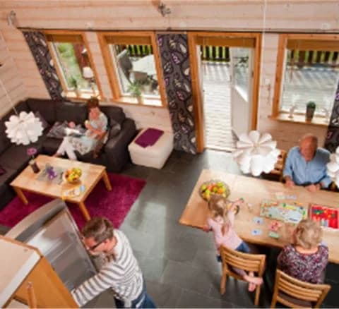 En mysig timmerstuga i Orsa Grönklitt omgiven av lummiga träd, med en liten veranda och mörk träfasad.