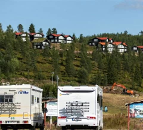En serie husvagnar och husbilar parkerade vid en campingplats i natursköna Orsa Grönklitt, omgivna av skog och berg.