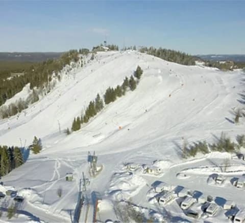 En snötäckt skidbacke i Orsa Grönklitt med barrträd som omger området, en typisk vinterscen med terrängens mjuka sluttningar och glaciärformationer synliga i bakgrunden.
