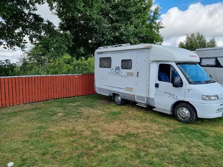 En husbil och en husvagn är parkerade vid Martins Rökeri och Camping med en grön gräsmatta runtomkring.