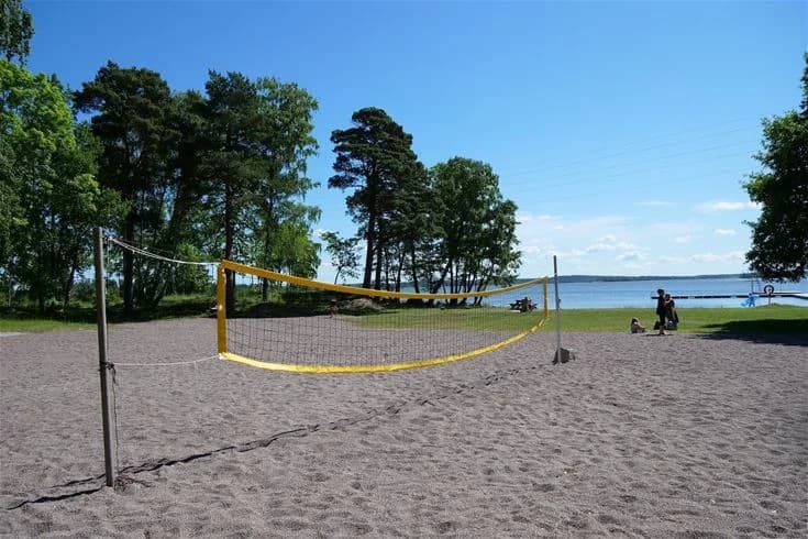En somrig strand vid Björknäs camping med en volleybollplan. I bakgrunden syns kustlinjen och ett soligt sommarlandskap.