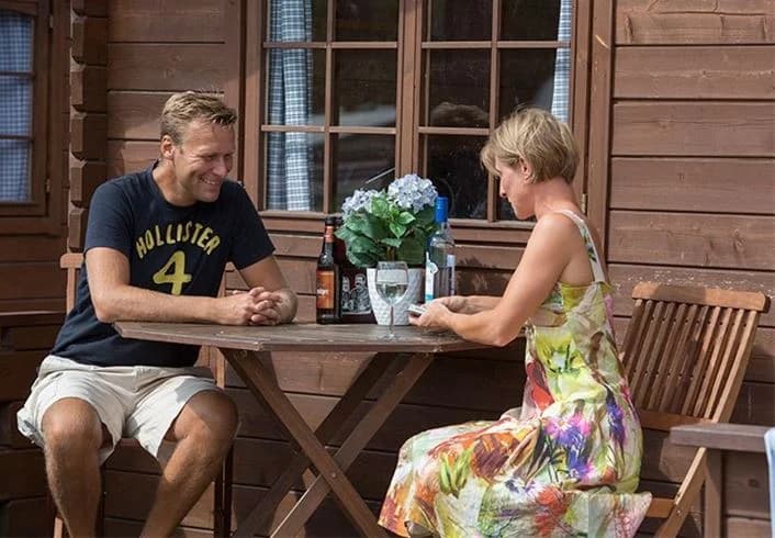 En somrig campingmiljö vid Borrbystrand med utemöbler i trä, en blomkruka och ett par i bermudashorts som njuter av ledighet.