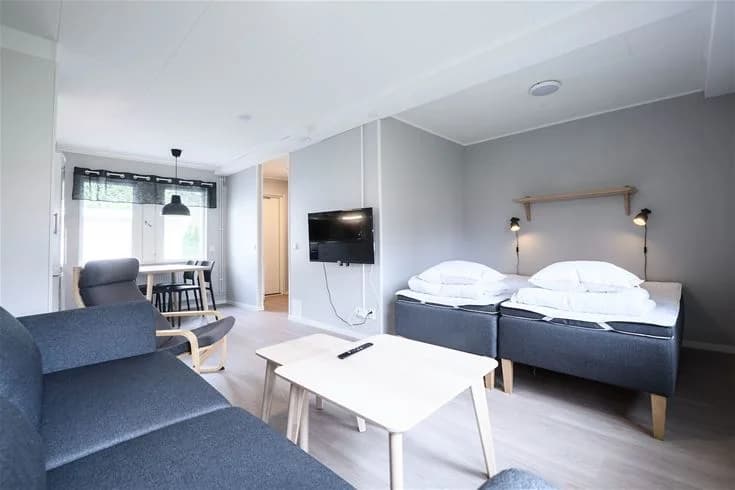 Ett rum på Östersunds camping med en inbjudande interiör. Rummet har ljusa väggar och tak, med en mysig säng placerad i mitten. Golvet är av trä, vilket ger en varm känsla. Möblerna är enkla men funktionella, och rummet framstår som hemtrevligt och välkomnande.