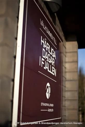 En skylt vid Åkersjöstrand Camping med företagets logotyp synlig. Texten har en lättläst font och kampanjarbete avspeglar genom en grafisk design som påminner om reklam eller ett banner.