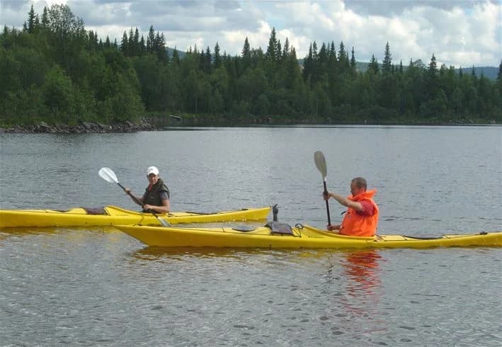 Personer paddlar kajak på en sjö nära Åkersjöstrand Camping, med kringliggande landskap i bakgrunden.