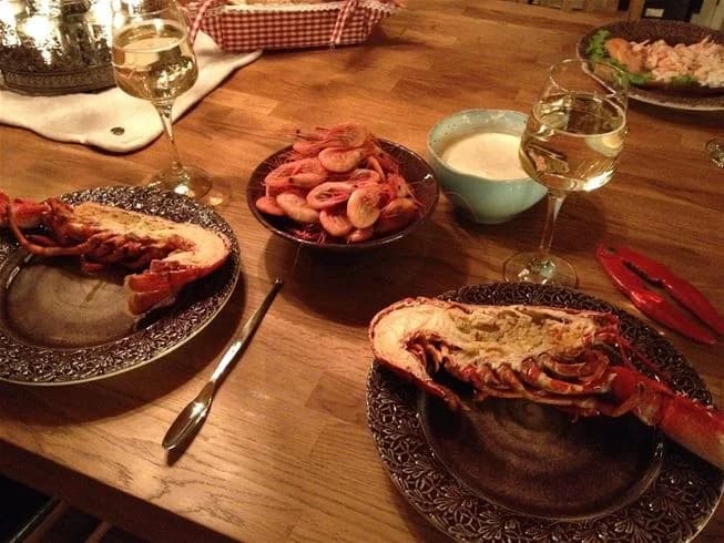 En uppdukad utomhusmiljö på Wiggersviks camping med ett bord fyllt av olika maträtter, inklusive skaldjur och kött. Tallrikar, glas och bestick är utplacerade för en måltid.