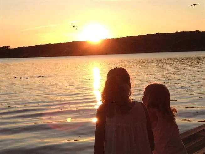 En solnedgång vid vattnet på Wiggersviks camping, där solens strålar färgar horisonten i varma sommartoner.