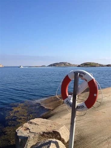 En livboj hänger vid kusten med havet i bakgrunden. I fjärran syns en ö och några båtar flyter på vattnet vid den natursköna stranden vid Wiggersviks camping.
