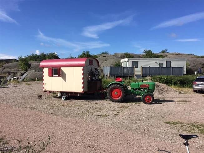 En campingplats med flera husvagnar och husbilar parkerade på rad, omgivna av grönska och träd. I bakgrunden syns en förrådsbyggnad och ett par stora husbilar, typiska för Wiggersviks Camping.
