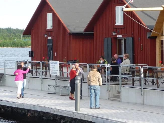 En träpir sträcker sig ut i vattnet vid Västra kajen camping, omgiven av båtar och bryggor i en stillsam marina.