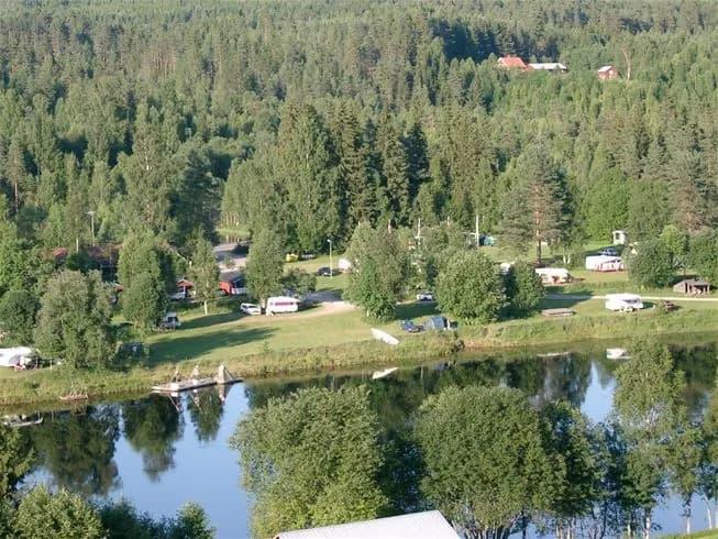 Flygbild över Värnäs camping som visar ett frodigt grönområde med tältplats, omgiven av skog och nära vattendrag.