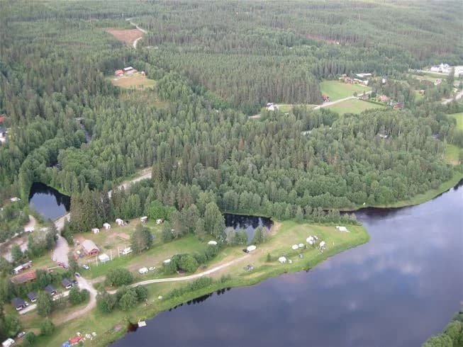 En naturskön vy vid Värnäs Camping med en klar sjö omgiven av grönskande träd och en lugn strand.