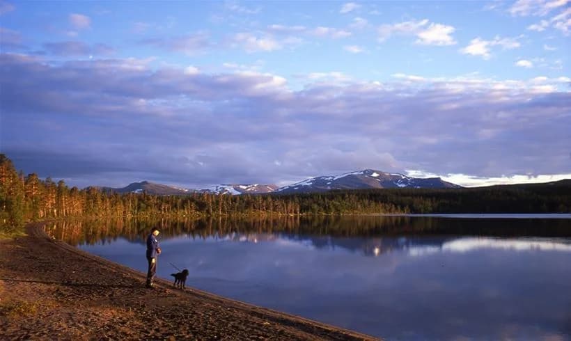 En vacker vy över ett spegelblankt vattendrag omgiven av berg och moln. I bakgrunden syns höglänta bergsformationer och vildmark, vilket skapar en rofylld och naturskön atmosfär vid Vålågårdens värdshus & camping.