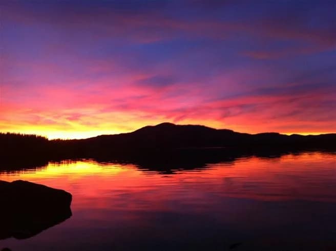 En idyllisk solnedgång över en sjö vid Vålågårdens värdshus & camping, med himlen färgad i olika nyanser av blått, rött och orange som speglas i det stilla vattnet.