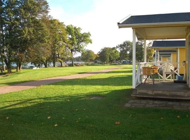 Bild av Vadstena camping. En grön gräsyta med träd som ger skugga. Området är öppet och inbjudande, med välskötta gräsmattor, typisk för en park eller trädgård, perfekt för camping och utomhusaktiviteter.