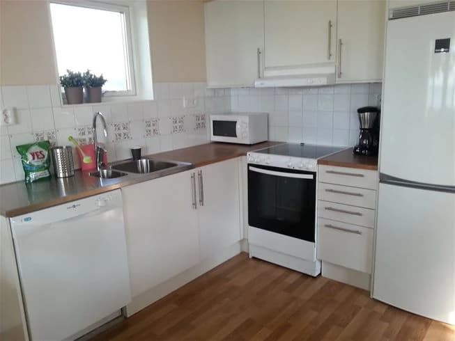 Ett fullt utrustat kök vid Vadstena camping med träinredning, inklusive skåp och bänkskiva. Kökets design har en hemtrevlig atmosfär med moderna hushållsapparater och trägolv.