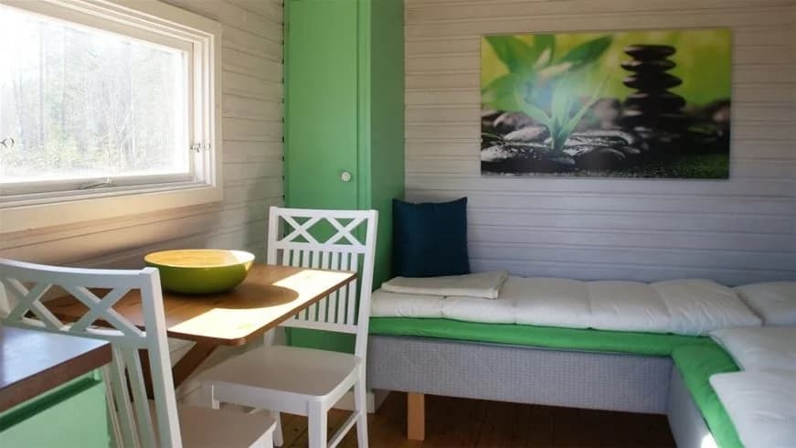 En mysig stuga med träinredning på Sörälgens camping. Stugan har ett trägolv, träpaneler på väggarna och ett tak med synliga träbjälkar. Det finns enkla möbler i rummet som matchar den naturliga och rustika stilen.