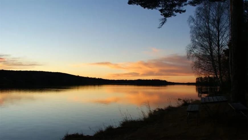 Bild av Sörälgens camping vid solnedgången. Vacker natur med en vattenväg som sträcker sig genom landskapet, himlen färgas av skymningens varma toner.