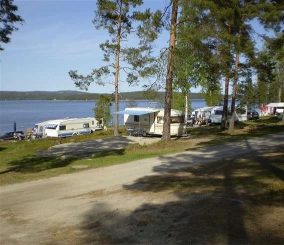 Bild av en kustlinje vid Sälstens Camping med ett glittrande hav som sträcker sig mot horisonten. Sandstranden övergår i klippor, och i fjärran syns en båt som glider över vattnet.