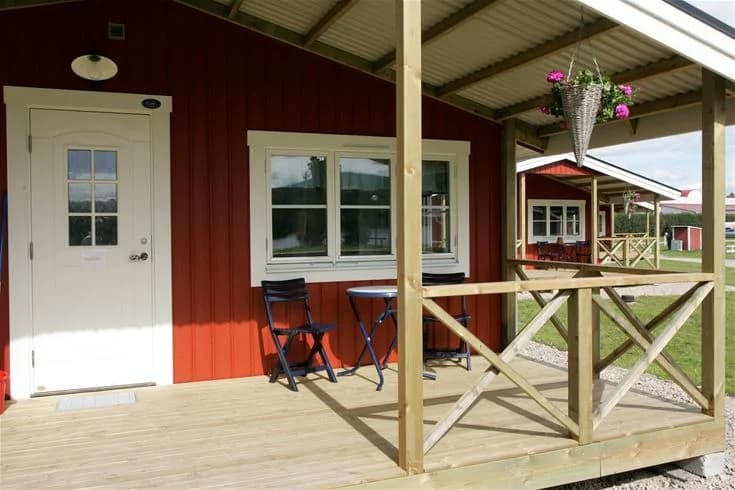 En trästuga med en veranda och utemöbler, omgiven av en grönskande trädgård på Sveg camping.
