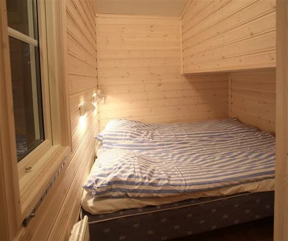 Bild av ett mysigt sovrum på Svegs Camping. Rummet har träinredning med bruna trädetaljer, ett trägolv och en säng med vita sängkläder.