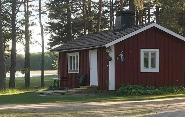 En liten trästuga med sadeltak omgiven av grönskande natur vid Strandstuvikens havsbad & camping.