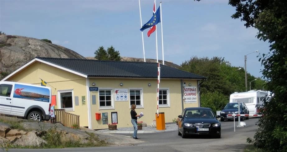 En överblick av parkeringsområdet vid Sotenäs Camping, med bilar parkerade på grusytan och omgivande grönska.