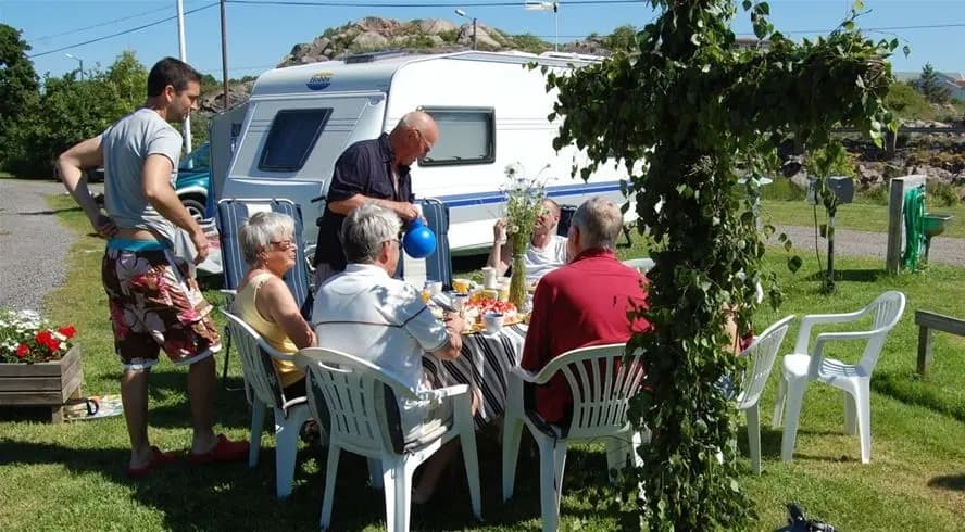 Bild av Sotenäs Camping som visar en gemytlig campingmiljö med husvagnar och husbilar. Fritidsmöbler som bord och stolar är placerade utomhus, vilket inbjuder till avkoppling och social samvaro i semestermiljön.