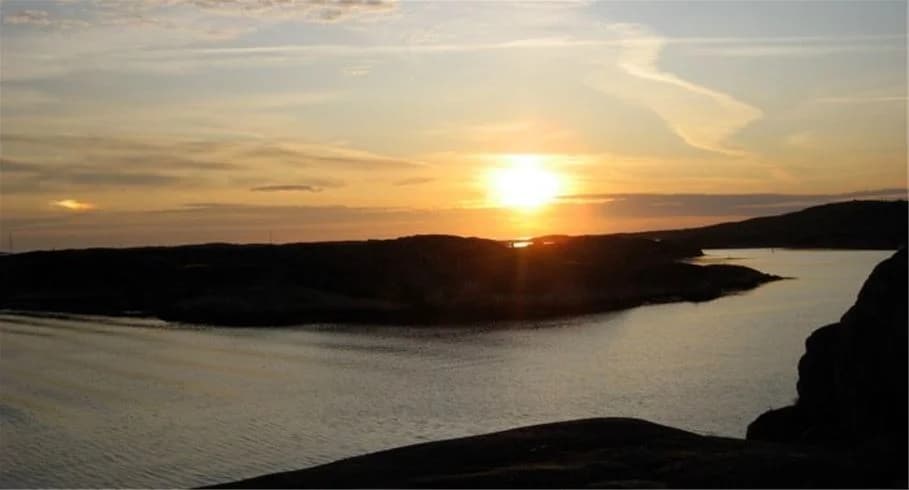 En vacker solnedgång vid Sotenäs camping med himlen färgad i varma toner. Siluetten av horisonten speglas i det lugna vattnet, vilket skapar en fridfull och avkopplande atmosfär.