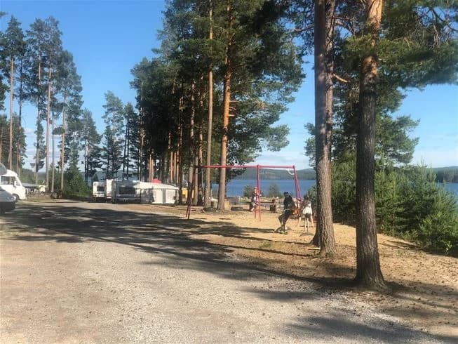 En solig dag vid Sandnäsets Bad & Camping med en vacker strandlinje och klarblått vatten, omgiven av frodig natur. Perfekt för avkopplande bad och campingupplevelser.