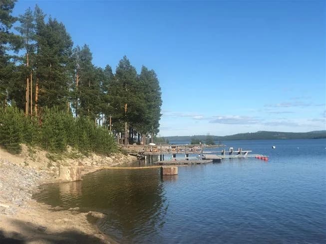 En vacker sjö med en sandstrand och campingområde i bakgrunden vid Sandnäsets bad & camping.