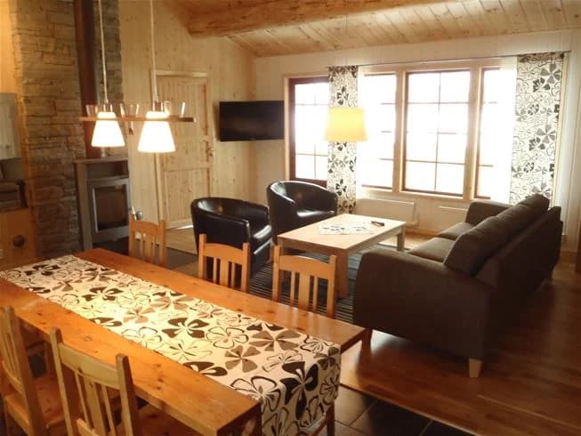 Ett inbjudande interiörfoto av en stuga på Saiva Camping & Stugby, med trämöbler, ett trägolv och ett träpaneltak som skapar en varm och rustik atmosfär. En träbord står i mitten av rummet, omgiven av olika sittmöbler.