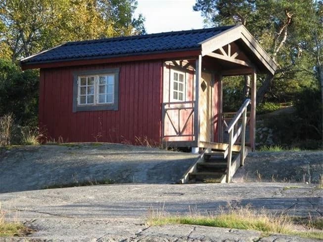 En träbyggnad på Rörviks camping, omgiven av grönska och träd. Byggnaden har en rustik och enkel stil, typisk för en stuga eller hydda.
