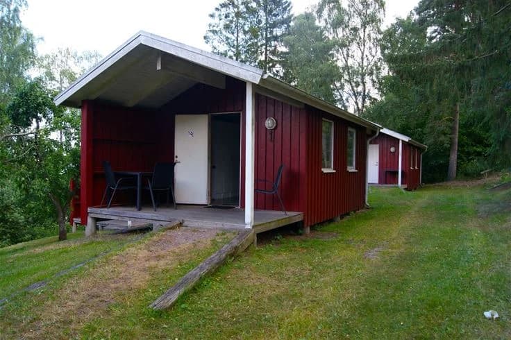 En mysig timmerstuga omgiven av gröna träd vid Orebackens camping, med en liten veranda och dörr i fokus.