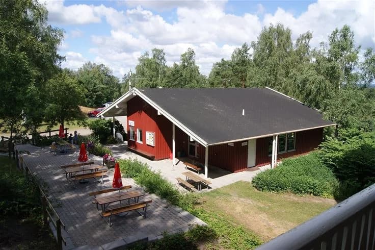 En välkomnande campingplats med stugor omgivna av en grön gräsmatta, skuggande träd och en lantlig atmosfär. Perfekt för rekreation och avkoppling i naturskön miljö.