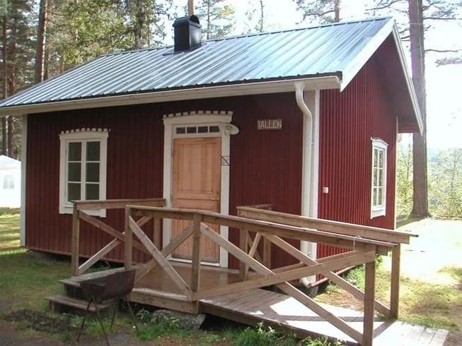 En trästuga på Näsåkers camping & stugby, med sidobyggnad och trappa, omgiven av grönska.