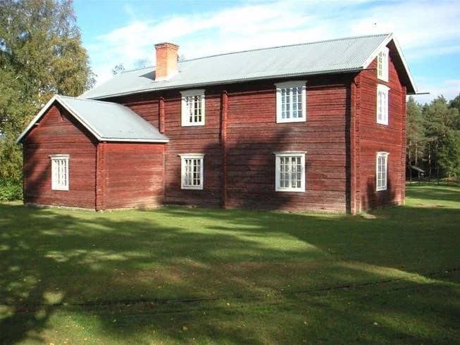 Bild av en pittoresk stuga på Näsåkers camping & stugby, omgiven av grönt gräs och ett lantligt landskap. Stugan har ett klassiskt sadeltak, fasad i trä och typiska spröjsade fönster, vilket skapar en charmig och avkopplande atmosfär.