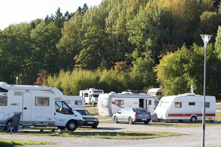 En parkering vid Norrtälje camping med flera husbilar och husvagnar uppställda, omgivna av träd och grönska.